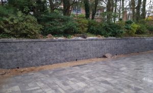 a paver driveway job in progress with a retaining wall and a green fence in Englewood Cliffs NJ 2