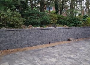 a paver driveway job in progress with a retaining wall and a green fence in Englewood Cliffs NJ