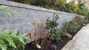 a paver driveway job with a retaining wall and a green fence in Englewood Cliffs NJ completed