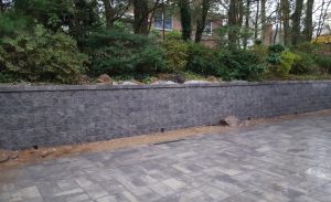 paver driveway in progress with paver retaining wall and green fence in Englewood Cliffs NJ